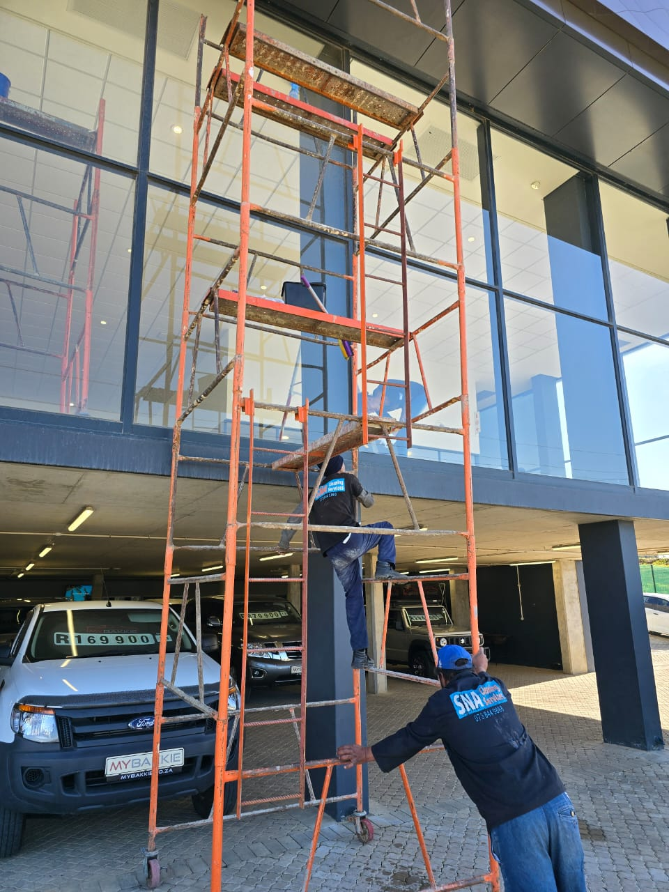 SNA cleaners on tall scaffolding washing a showroom facade